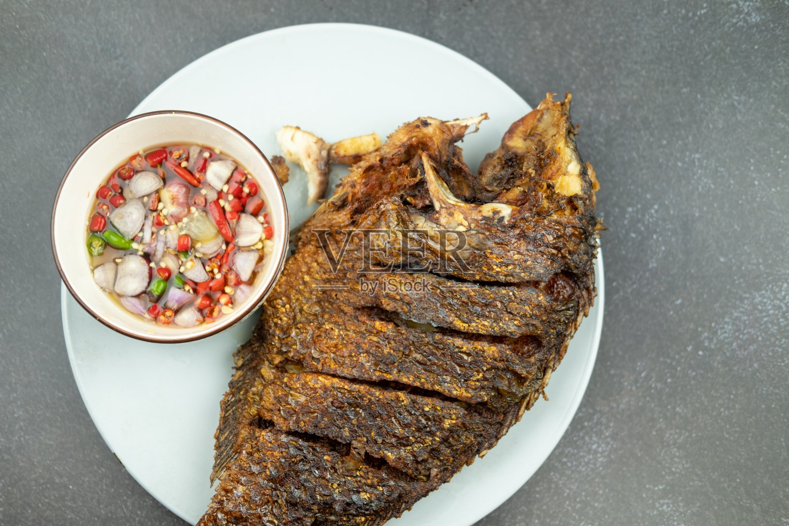 罗非鱼配辣酱油煎，白色盘子，黑色背景。照片摄影图片