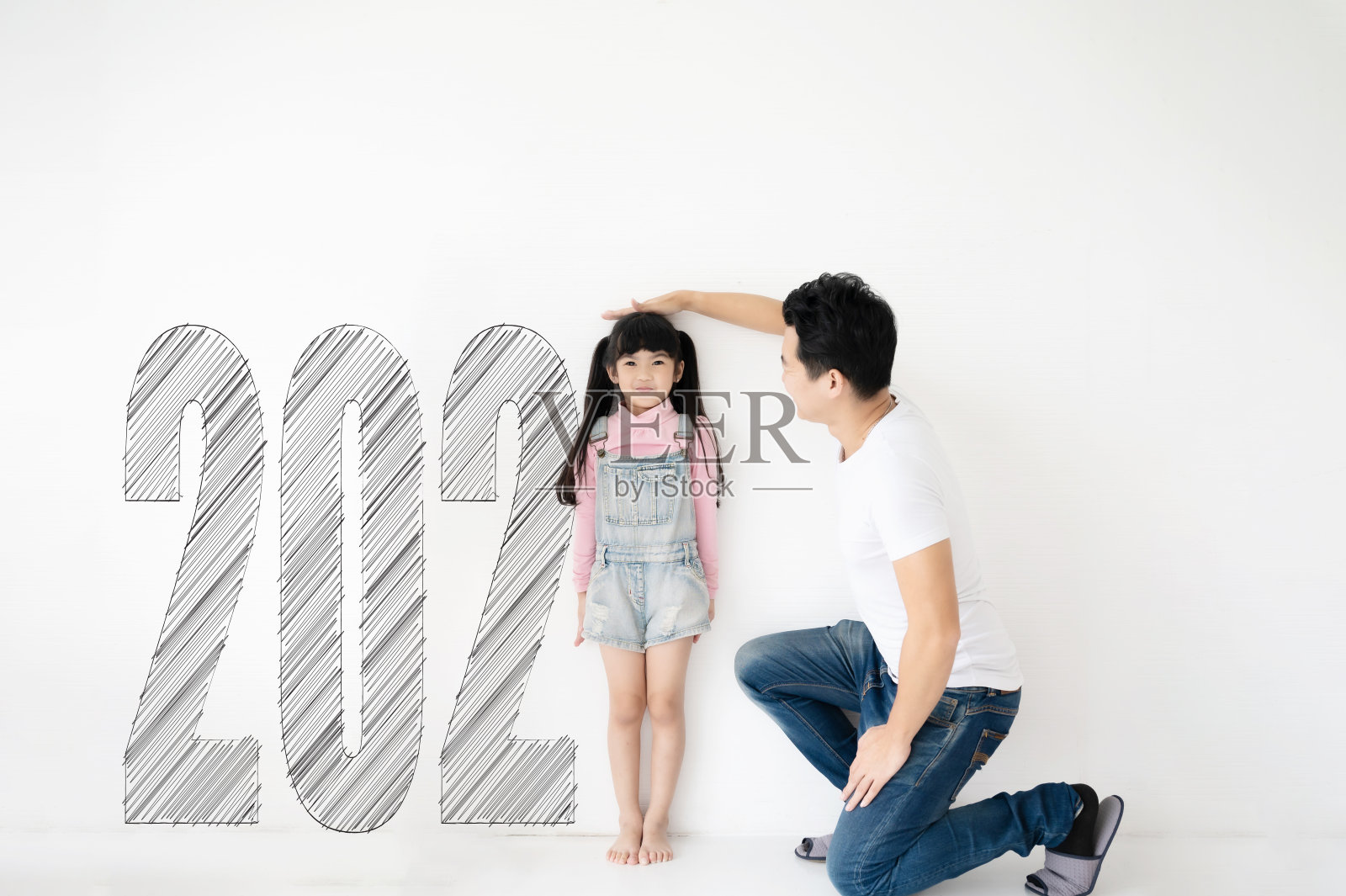 爸爸在白砖墙上测量女儿的身高增长，数字是2021年照片摄影图片