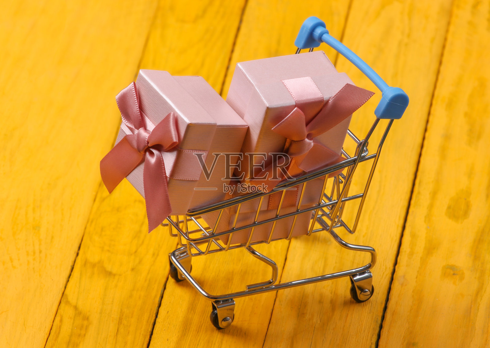 购物手推车和礼品盒与蝴蝶结在黄色的木制背景。照片摄影图片