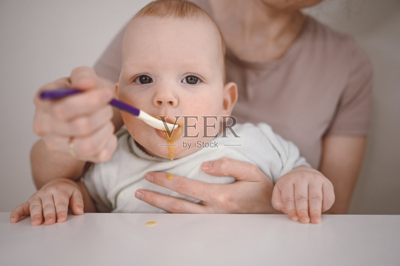 刚出生的有趣的小男孩正在学习用勺子从玻璃罐里吃蔬菜或水果泥。年轻的母亲帮儿子吃第一顿饭。照片摄影图片