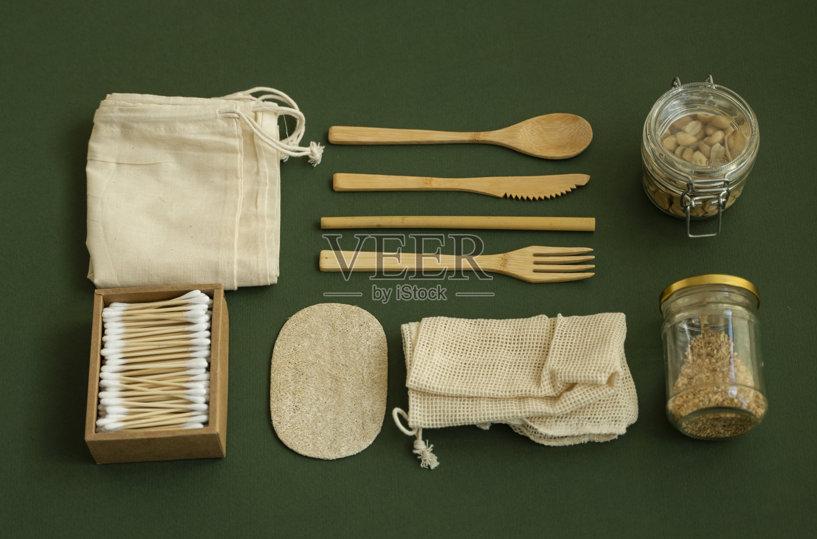 “零浪费”。一套环保竹餐具，网眼棉袋，玻璃罐一个坚果，丝瓜海绵和棉签盒。自然和可重复使用的物品配件在绿色表面。照片摄影图片