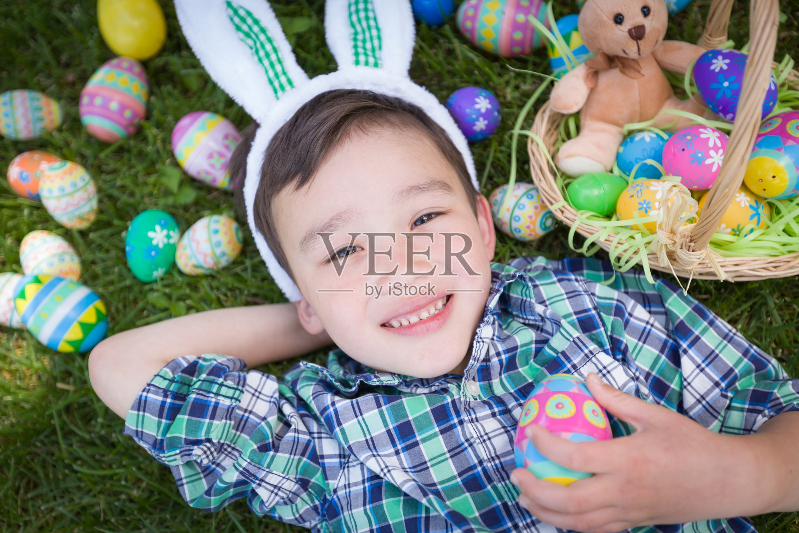 混血儿中国人和白种人男孩戴着兔子耳朵在外面玩复活节彩蛋照片摄影图片