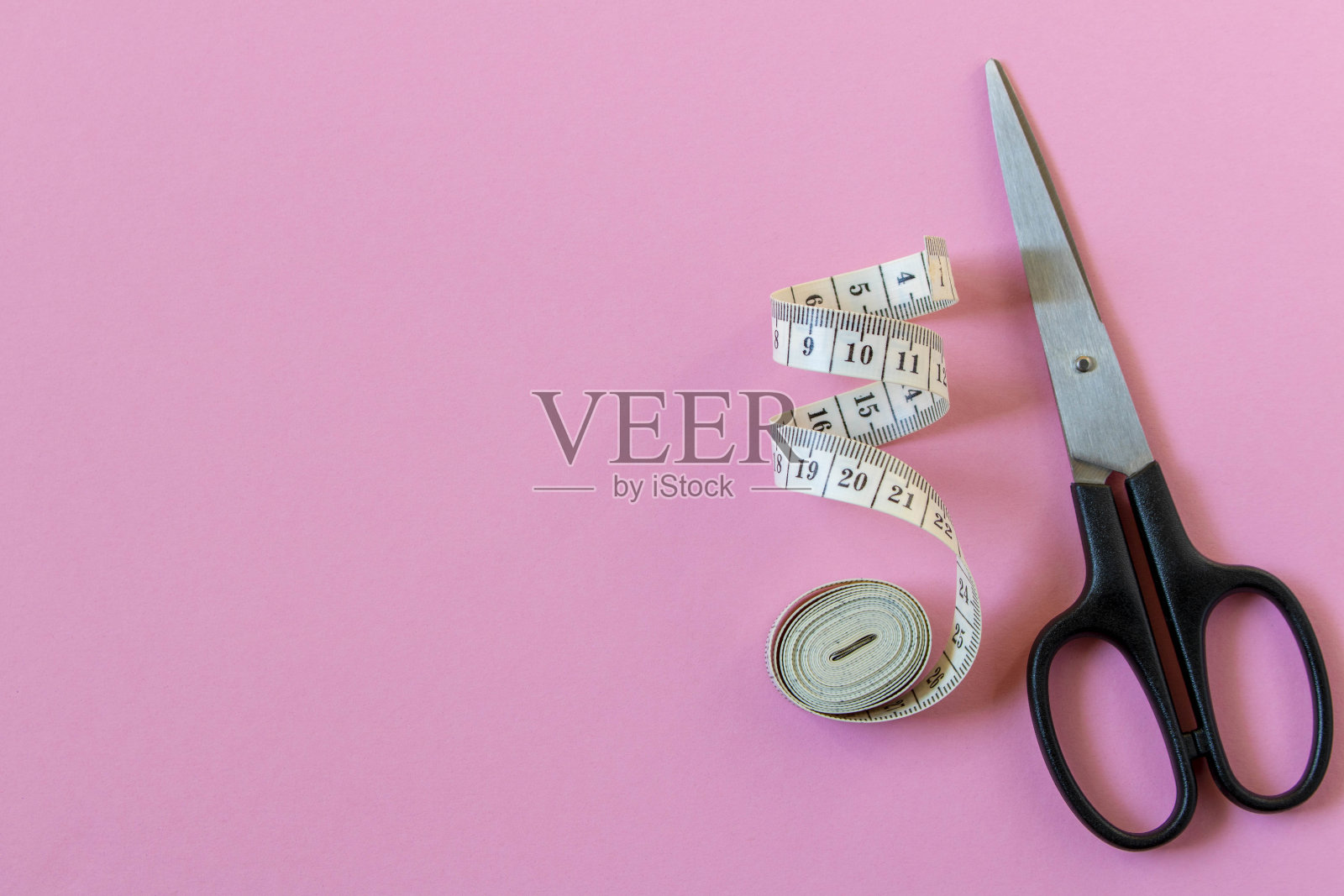 粉色背景上的白色卷尺和剪刀。特写镜头。照片摄影图片