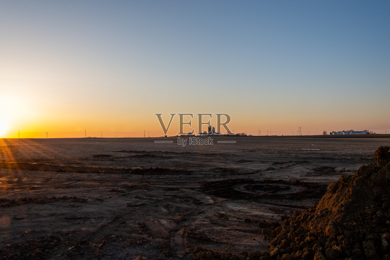 在晴朗无云的天空下，夕阳照亮了远处的农场建筑。照片摄影图片