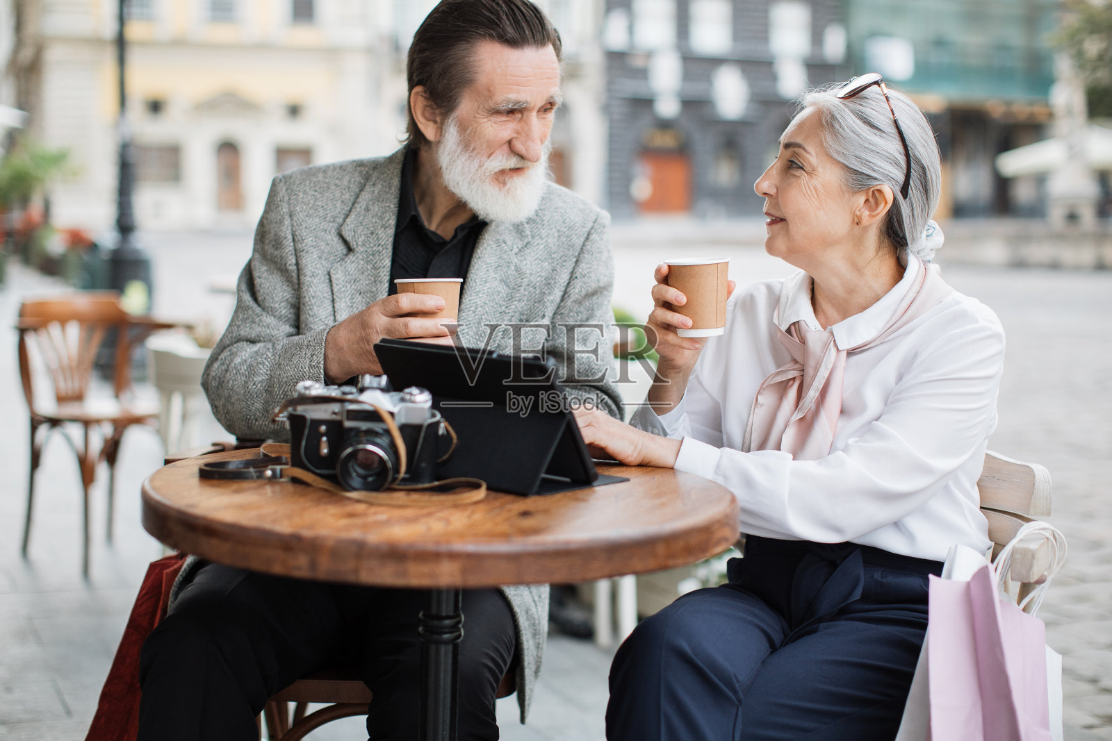年老的夫妇放松在咖啡馆露台与咖啡和平板电脑照片摄影图片
