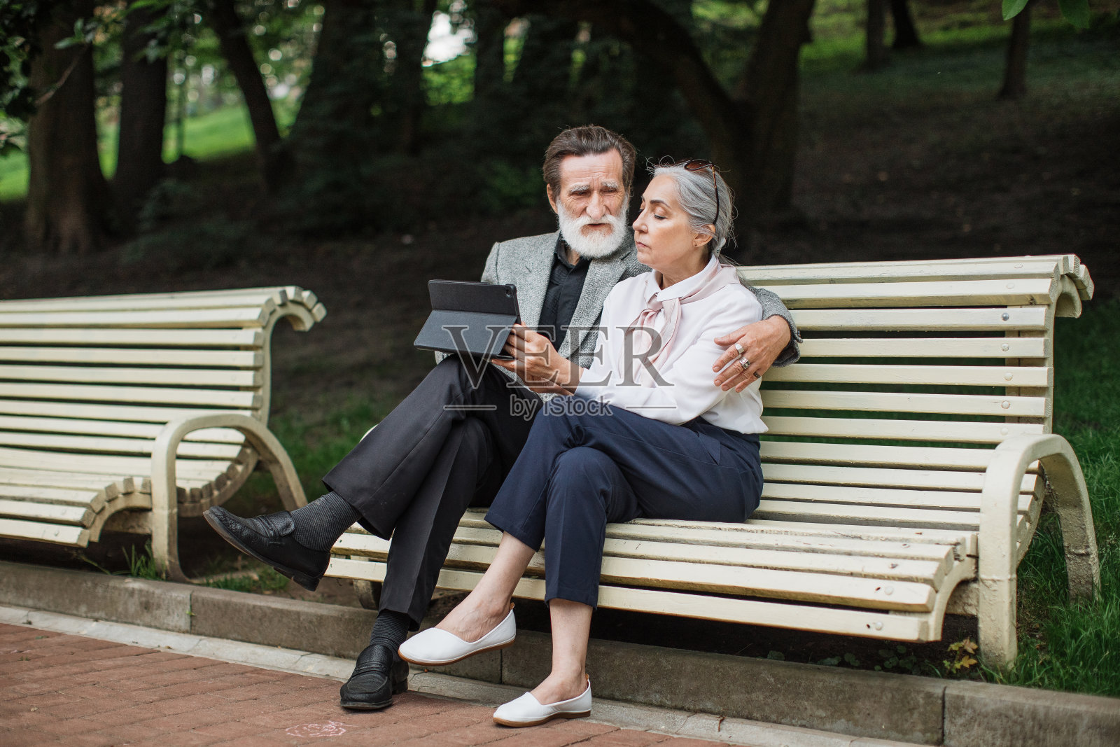 一对老年夫妇在长凳上休息，用着平板电脑照片摄影图片