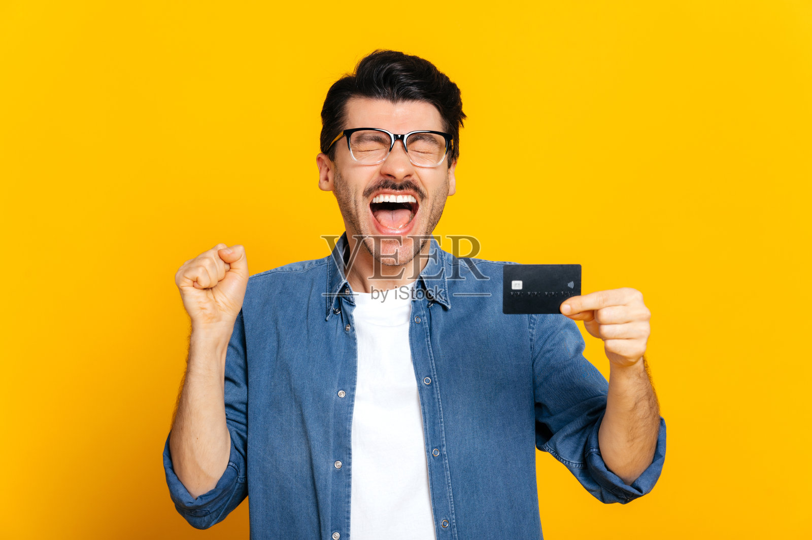 快乐开朗的白种人，不刮胡子的时尚的家伙拿着信用卡在手里，高兴地大喊，站在孤立的橙色背景，金融和银行的概念照片摄影图片