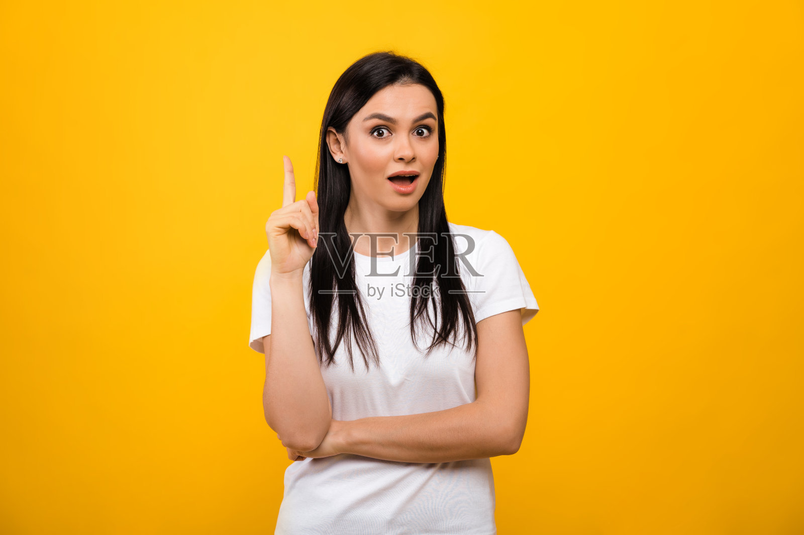 一个穿着白色基本t恤的相当兴奋的白人黑发女人，有了一个新的想法，站在孤立的橙色背景上，直视着摄像机照片摄影图片