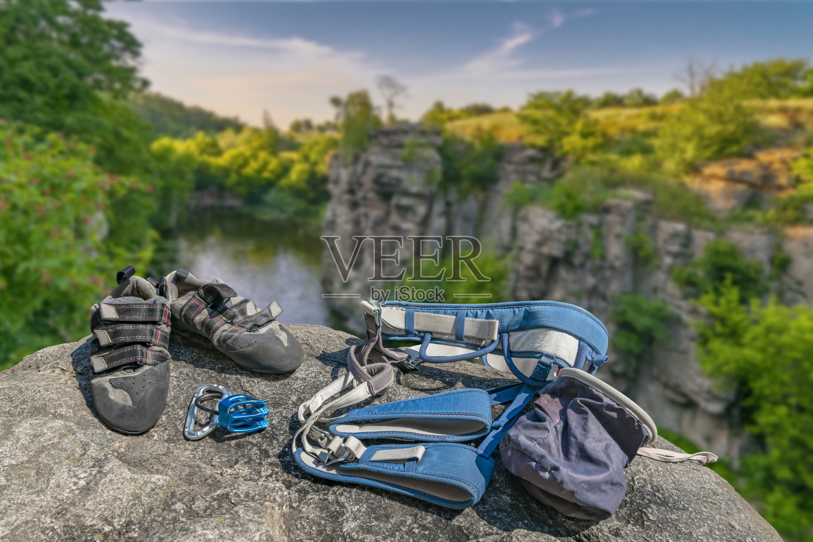 攀爬设备上的岩石上模糊的河流峡谷背景。攀爬鞋，确保钩，环，绳索，包，确保系统。照片摄影图片