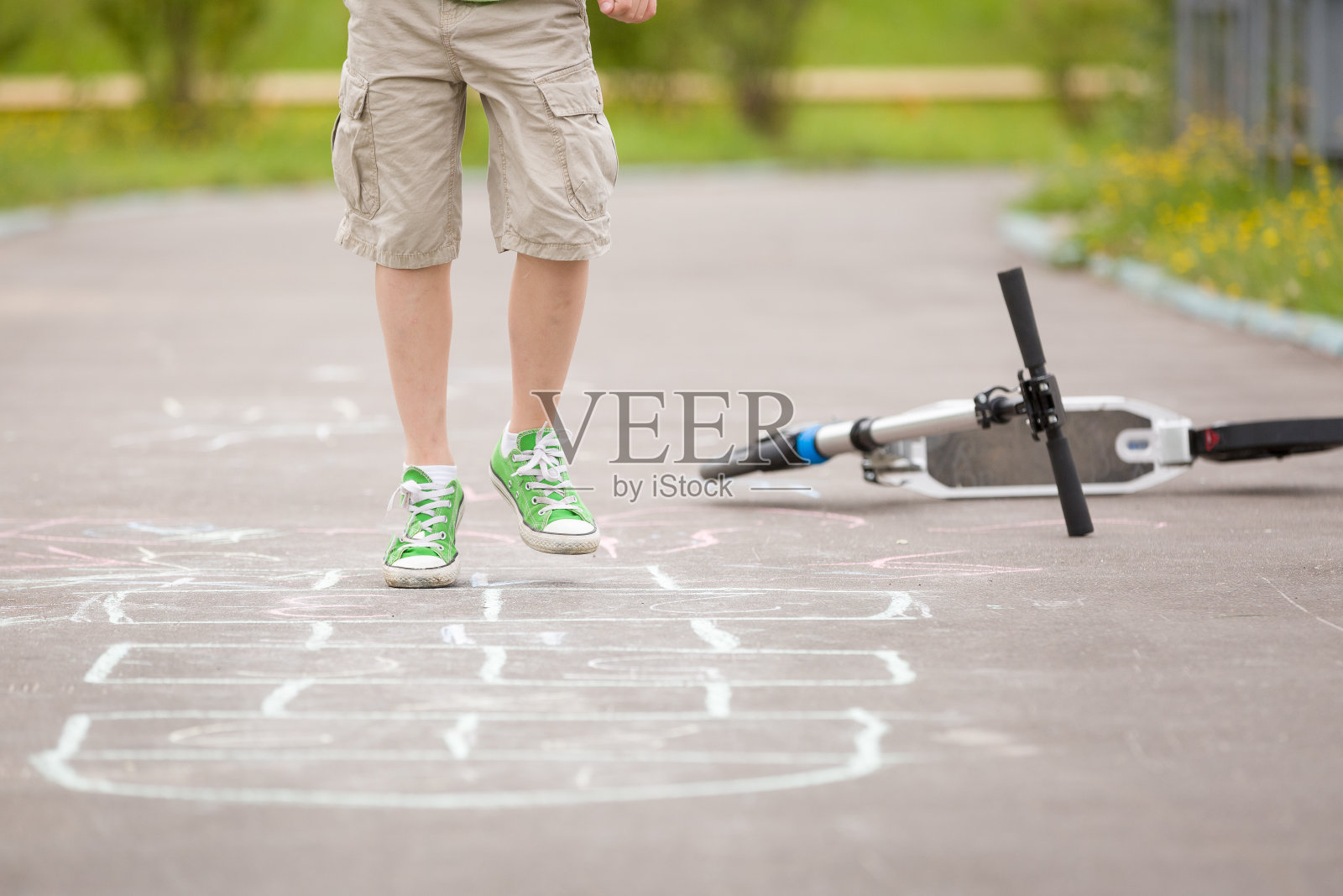 男孩的腿和在沥青上画的跳房子的特写。一个阳光明媚的日子，孩子们在户外的操场上玩跳房子游戏。儿童户外活动。照片摄影图片