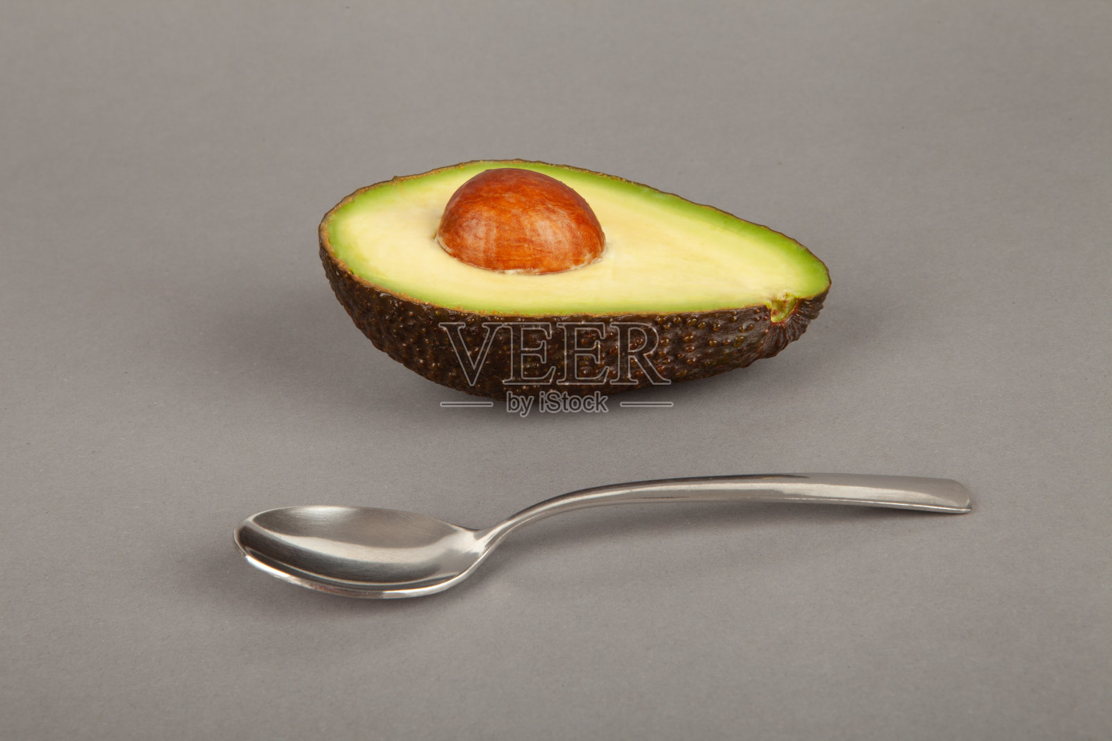 半只带骨头和勺子的鳄梨躺在灰色的背景上。照片摄影图片