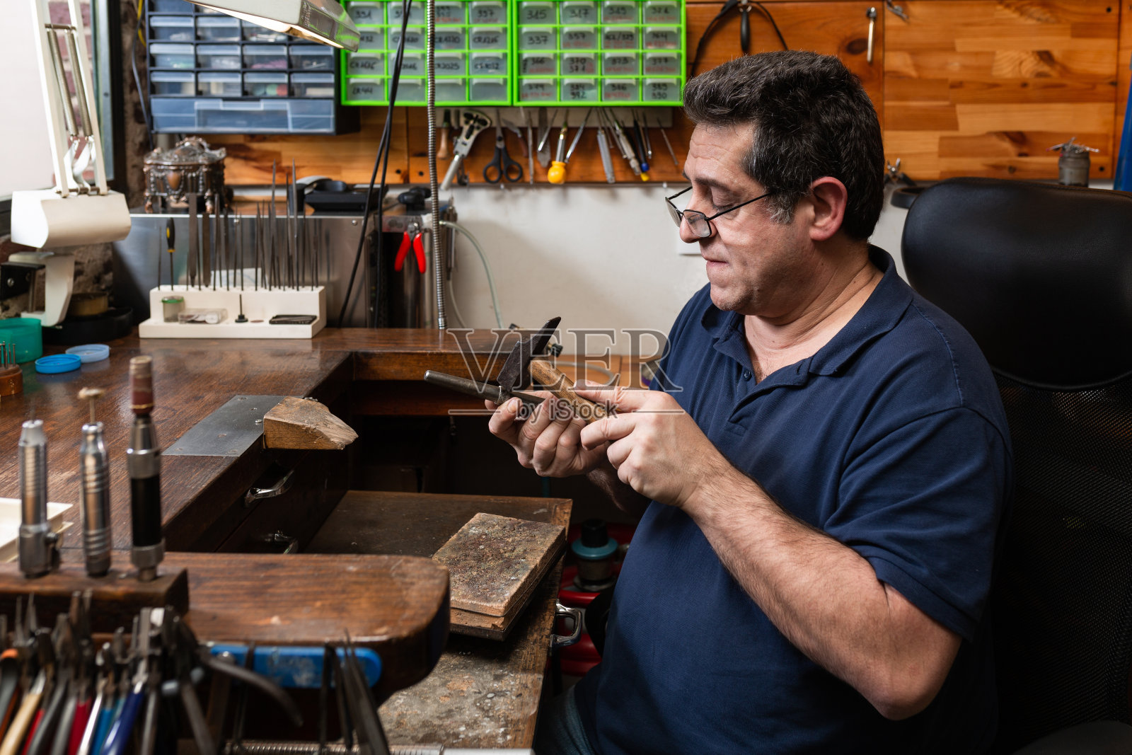 前景，锤子锤一个银戒指形状，在一个珠宝车间。照片摄影图片