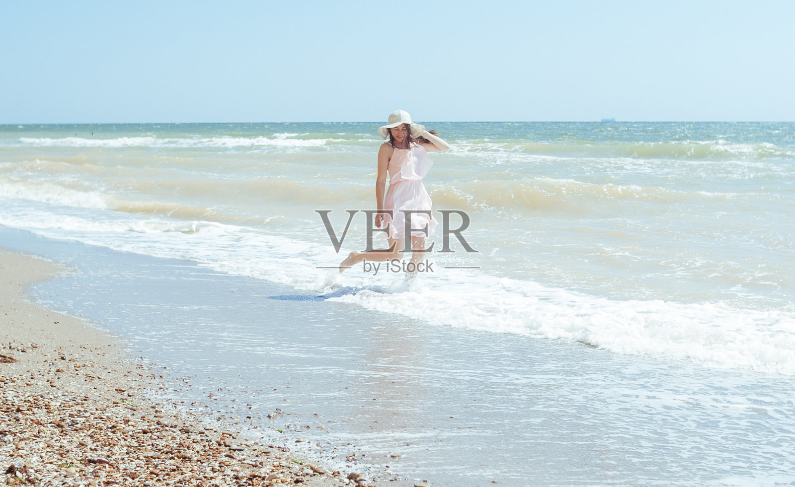 戴着帽子，穿着粉红色衣服的女孩在海浪上奔跑照片摄影图片