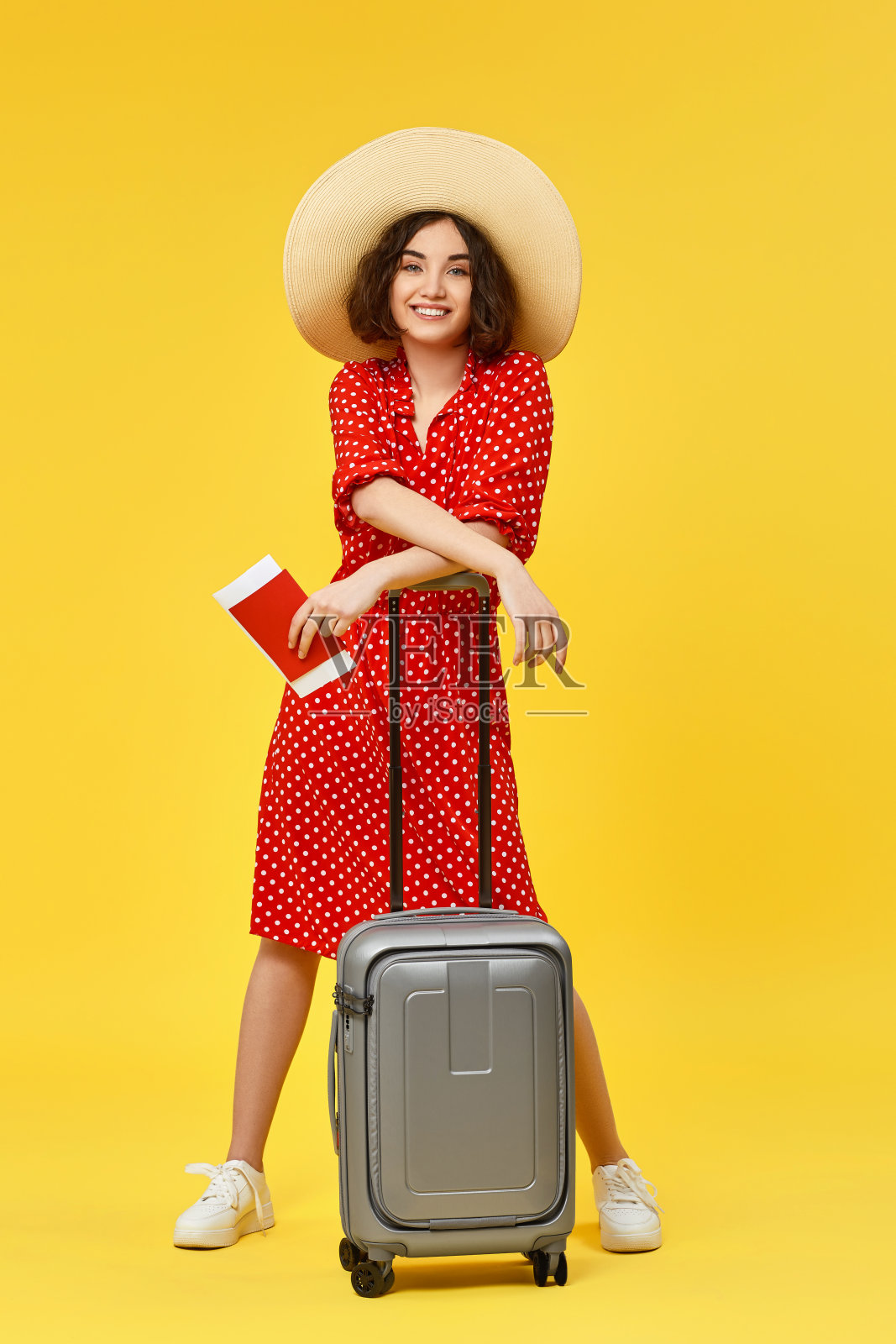 黄色背景下提着行李箱旅行的女人。照片摄影图片