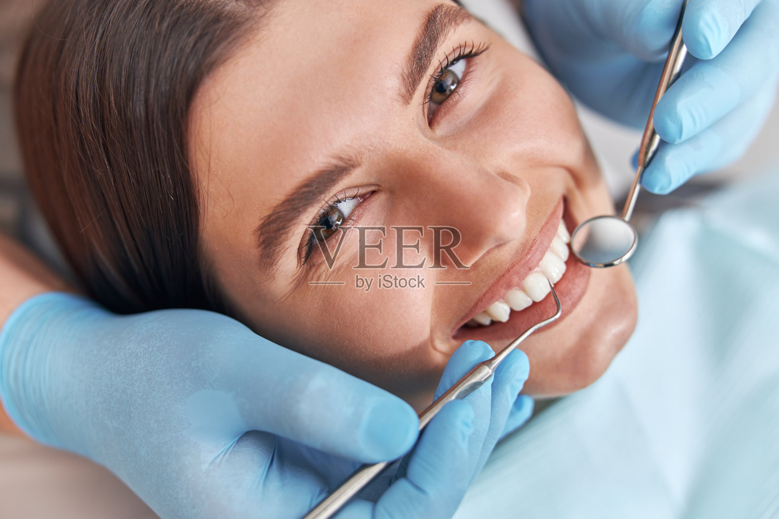 乐观积极的牙科病人。女性牙科病人在牙科手术，医生使用牙科仪器在现代牙科诊所照片摄影图片