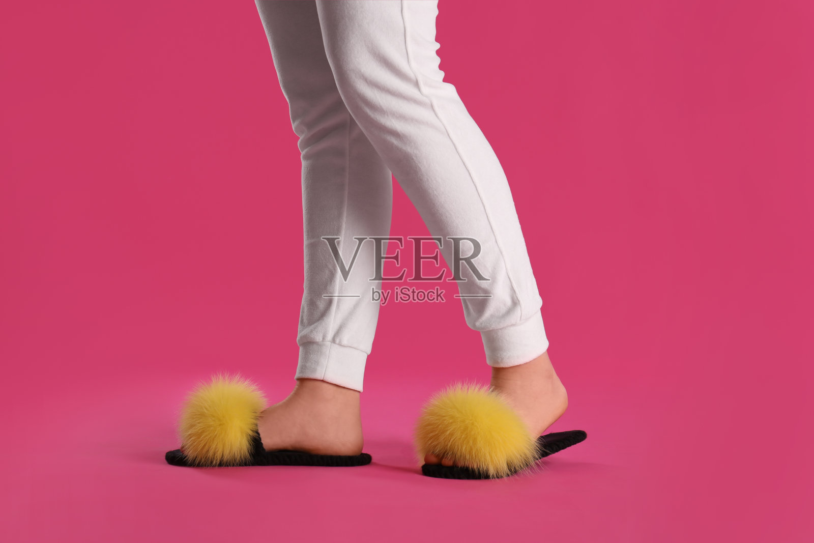 粉色背景上穿着毛绒拖鞋的女人，特写照片摄影图片