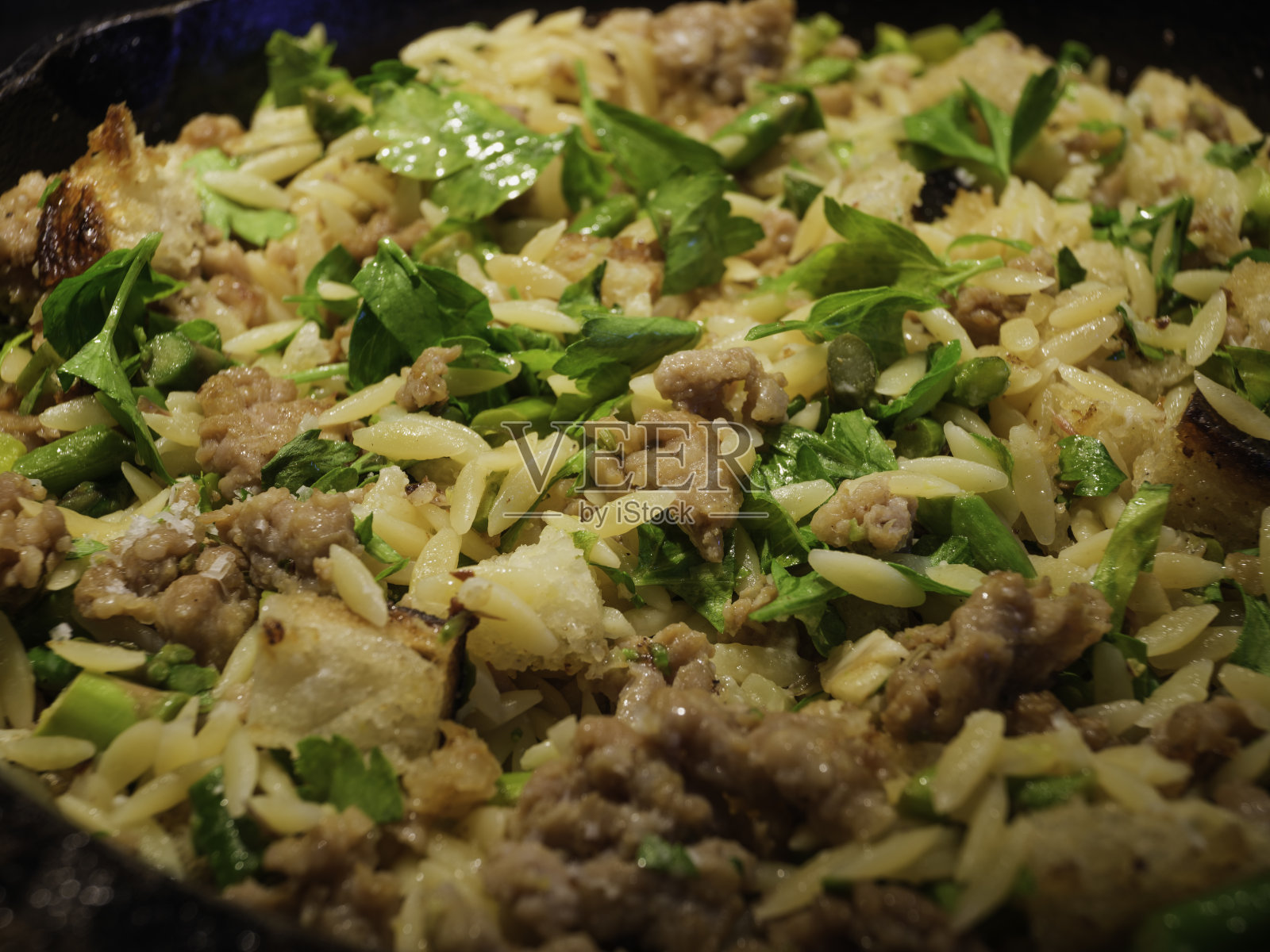 用黑色铸铁煎锅煮米粉。一锅煎锅晚餐，香肠，芦笋，米粉，面包屑。照片摄影图片