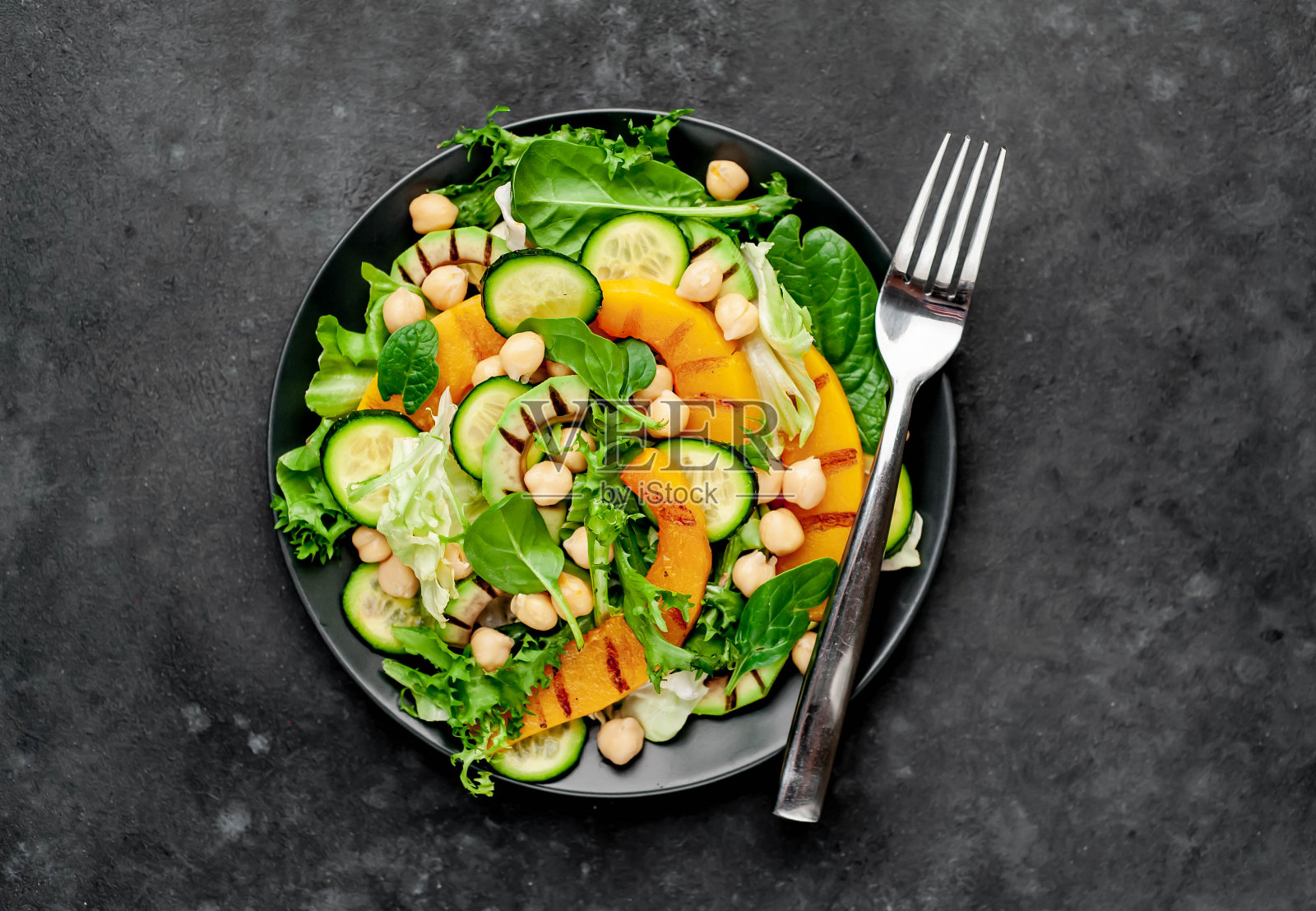 石头背景上放着一盘南瓜沙拉、鳄梨、黄瓜、鹰嘴豆和莴苣。照片摄影图片