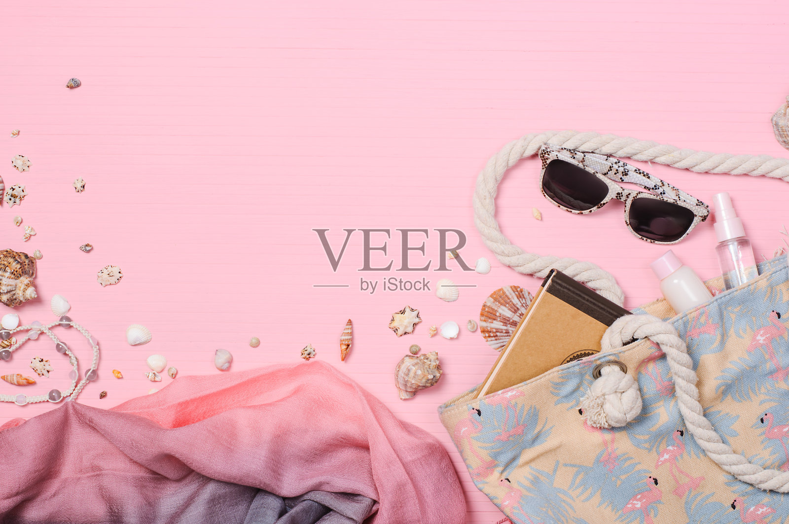 沙滩包，保湿霜，太阳镜，粉色背景上的贝壳，平躺着。暑假旅游度假背景，日光浴，沙滩配件照片摄影图片