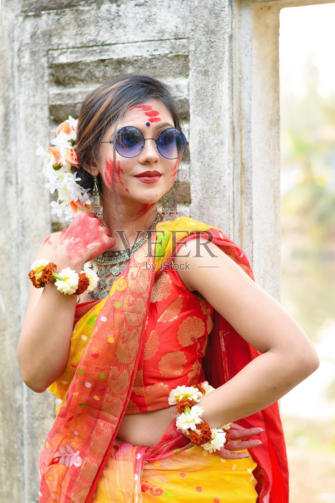 在被称为胡里节的色彩节上，漂亮的年轻印度女孩穿着传统纱丽和珠宝，玩弄颜色，戴着太阳镜摆出时尚的姿势。照片摄影图片