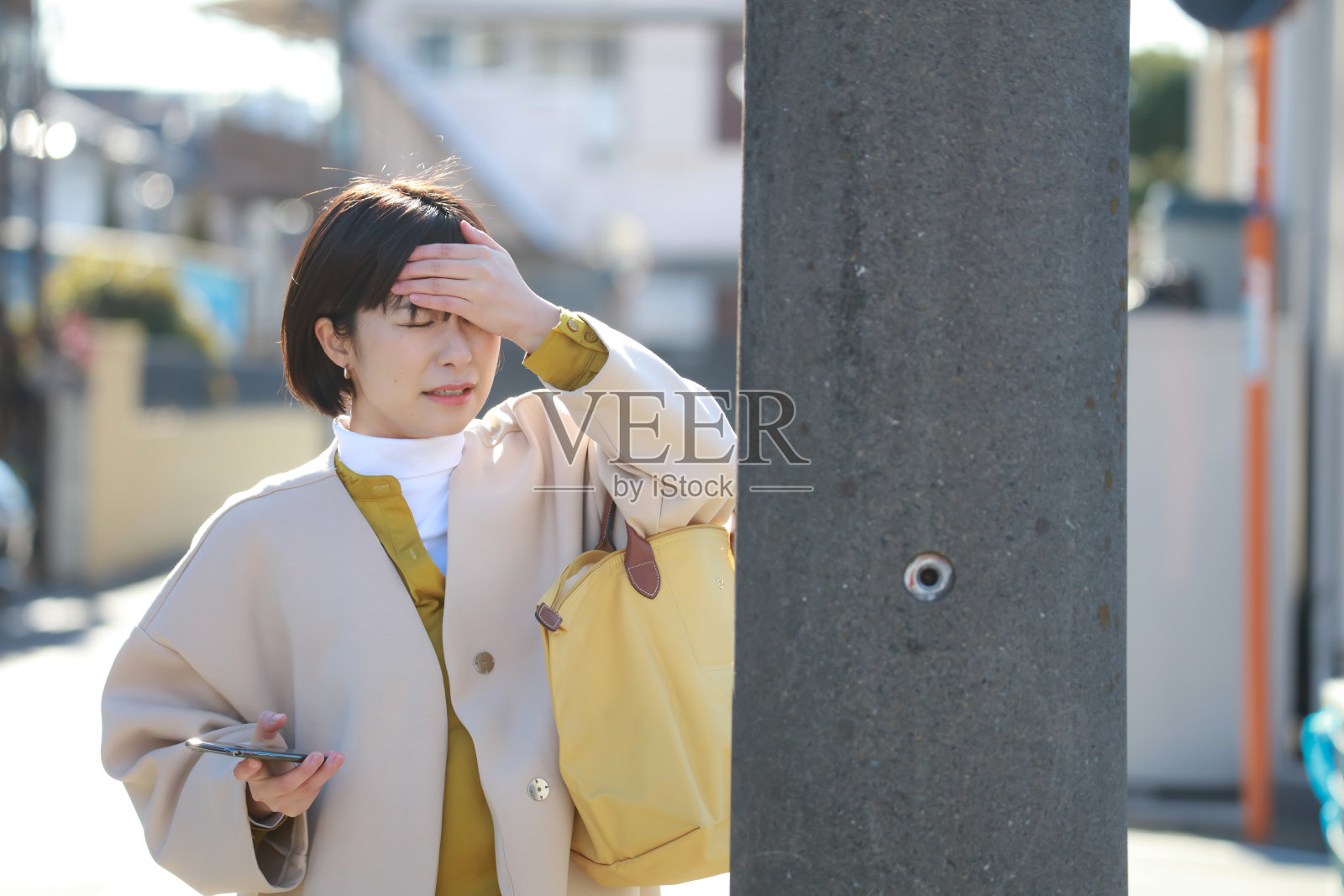 一个女人踩着智能手机走路，头撞到了电线杆上照片摄影图片