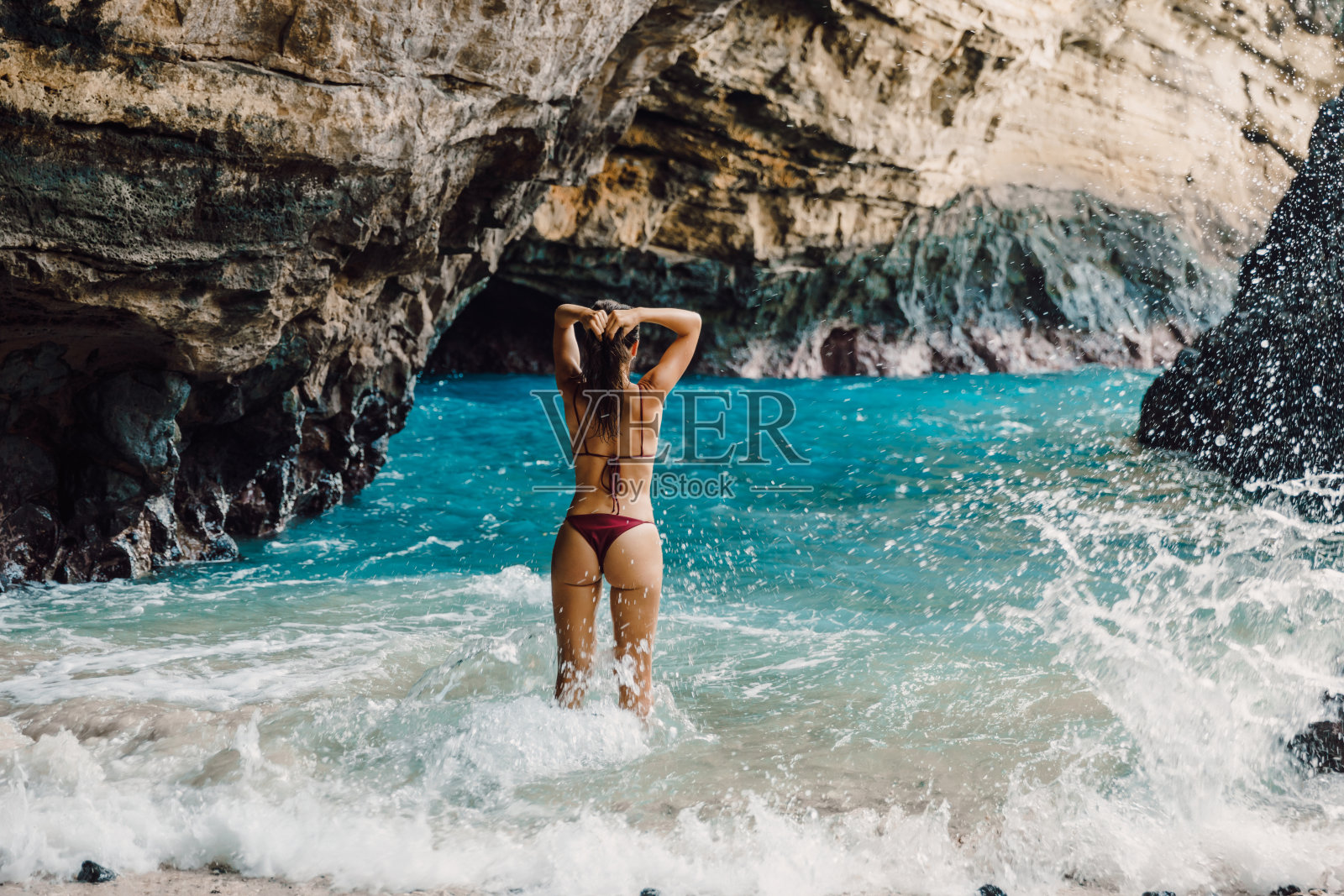 苗条的黑发女人在比基尼在沙滩摆姿势。晒黑的女模特度假照片摄影图片