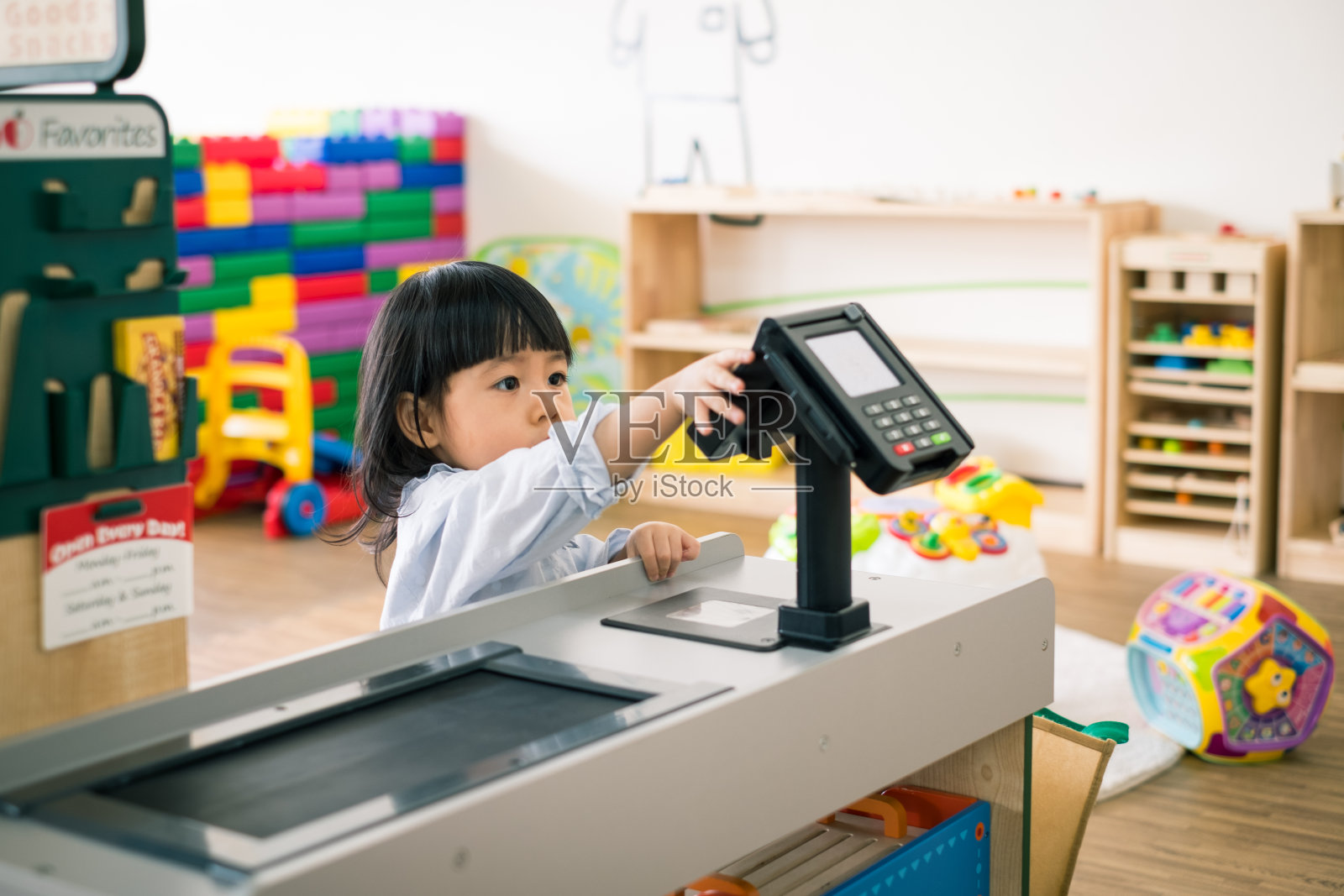 一个蹒跚学步的孩子在玩购物游戏，并触摸收银员付款。照片摄影图片