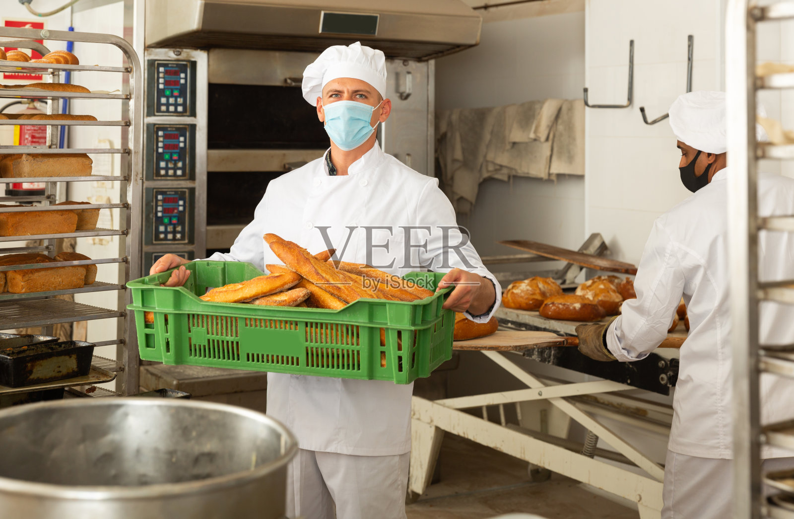 面包师的肖像在保护面具与新鲜面包在面包房照片摄影图片