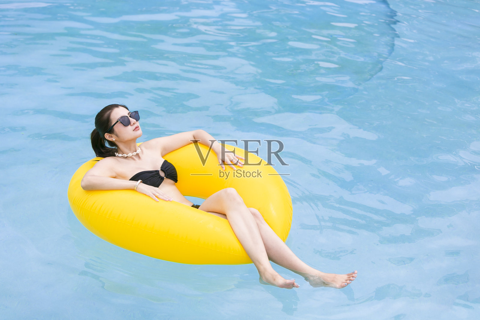 美丽的黑人女人，在游泳池的充气环上放着一杯夏日鸡尾酒。照片摄影图片