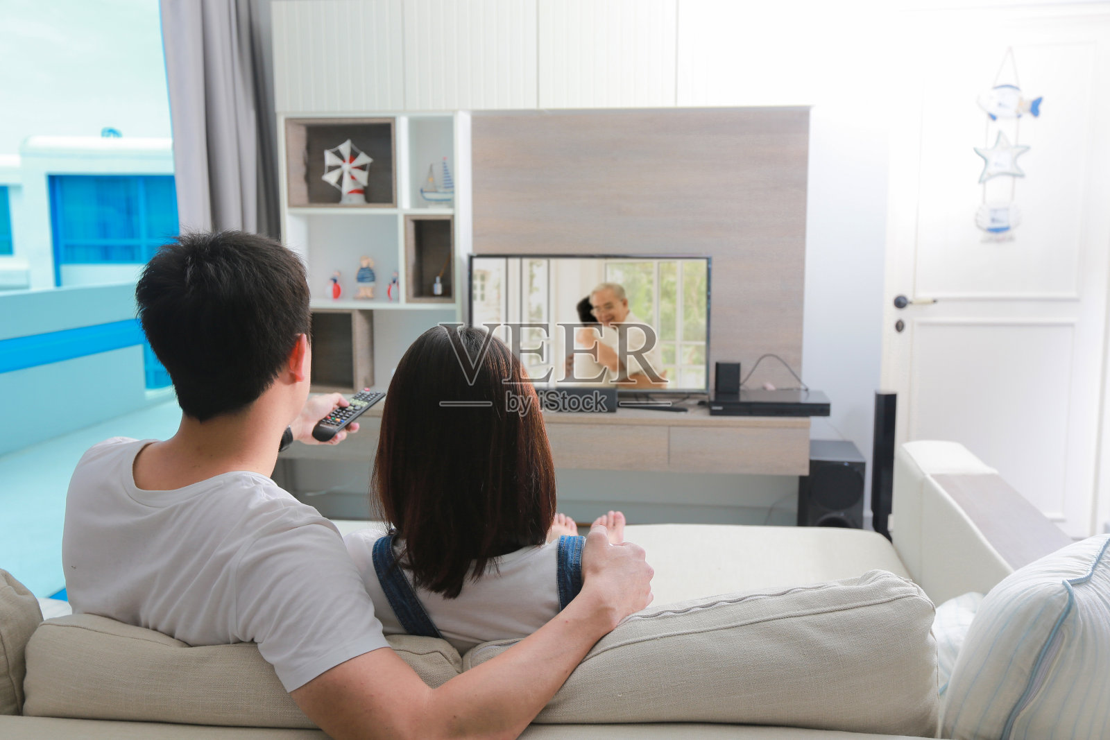 后视图情侣拥抱和坐在沙发上看电视在客厅。照片摄影图片