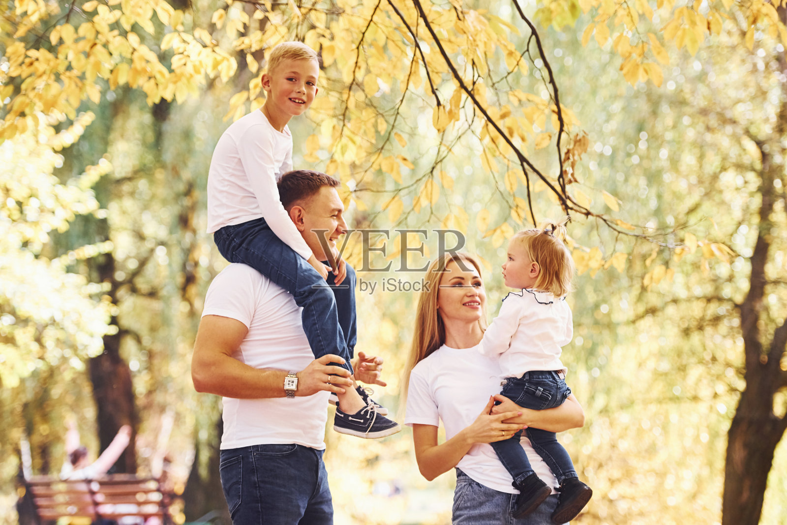 妈妈和爸爸把孩子放在肩膀和手里。快乐的年轻家庭一起在秋天的公园散步照片摄影图片