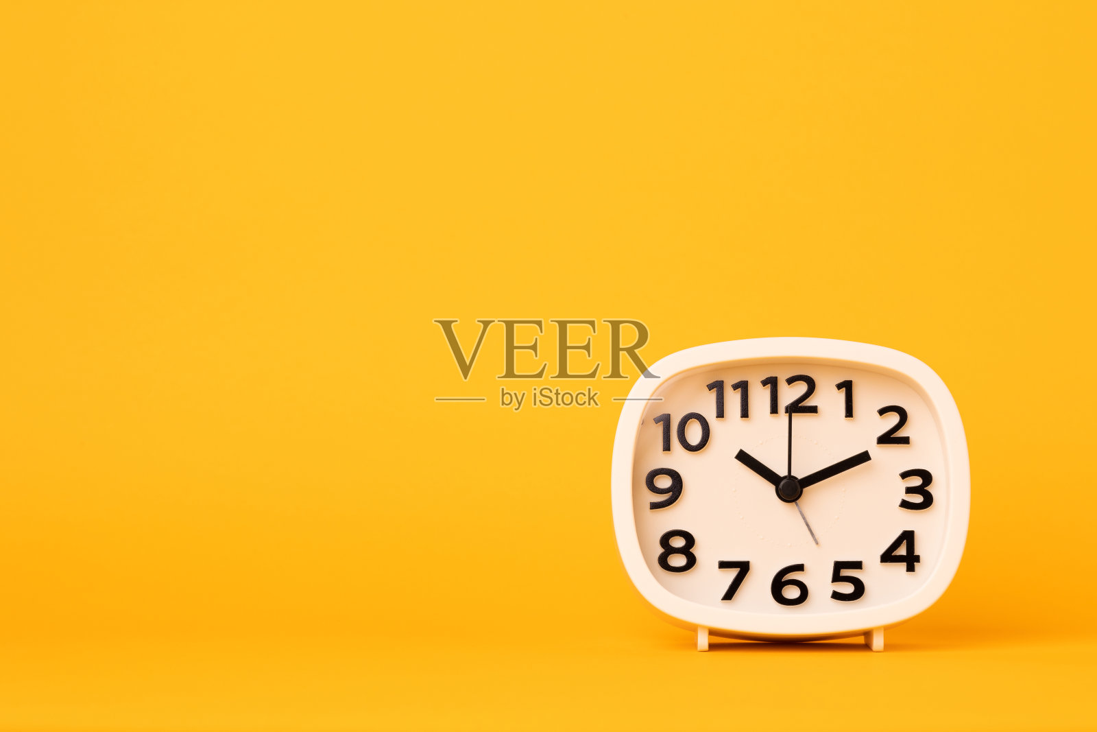 白色的小闹钟，黑色的数字，把设定好的时间放在桌上。时钟孤立黄色背景。照片摄影图片