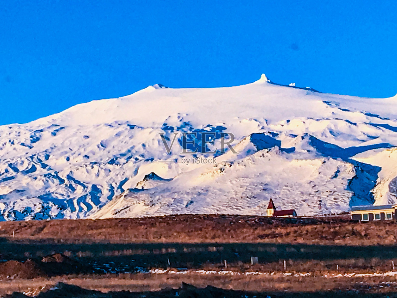一座巨大的雪山前的小教堂照片摄影图片