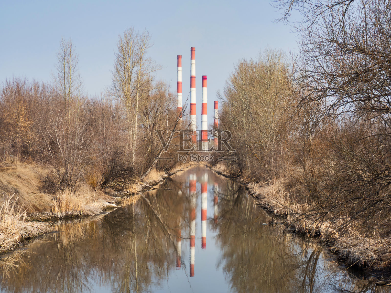 植物发电的水渠，水中反射的管道，晴天没有叶子的树木照片摄影图片