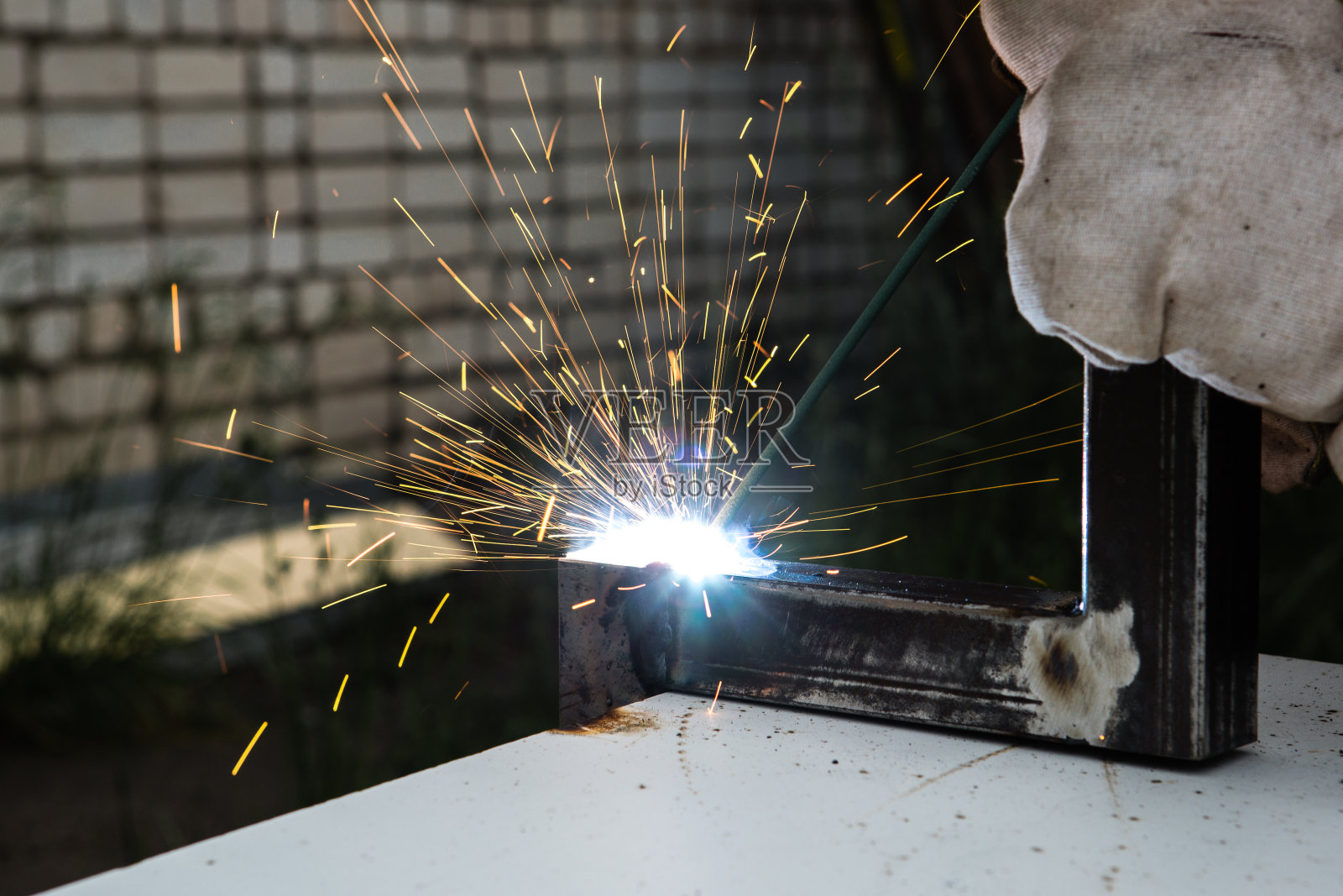 室外用焊机金属焊接一名带施工手套和焊接面罩的男子焊工。照片摄影图片