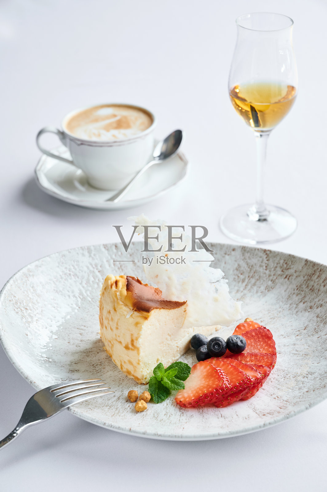 白盘子里有新鲜草莓和蓝莓的奶酪蛋糕，咖啡桌上有拿铁和一杯白兰地照片摄影图片