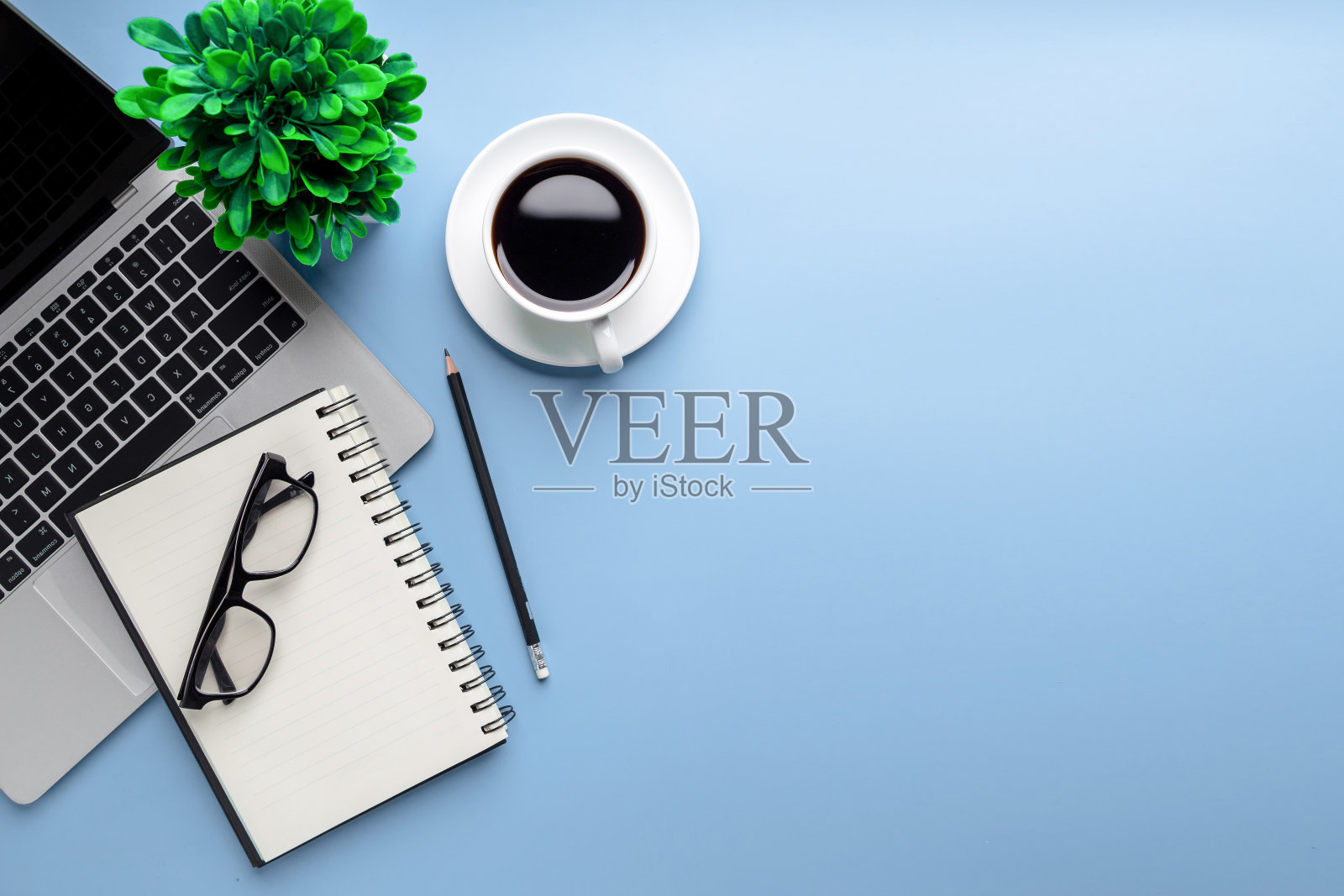 平躺，俯视图办公桌桌。工作空间，笔记本电脑，办公用品，铅笔，绿叶，和咖啡杯在蓝色的背景。照片摄影图片