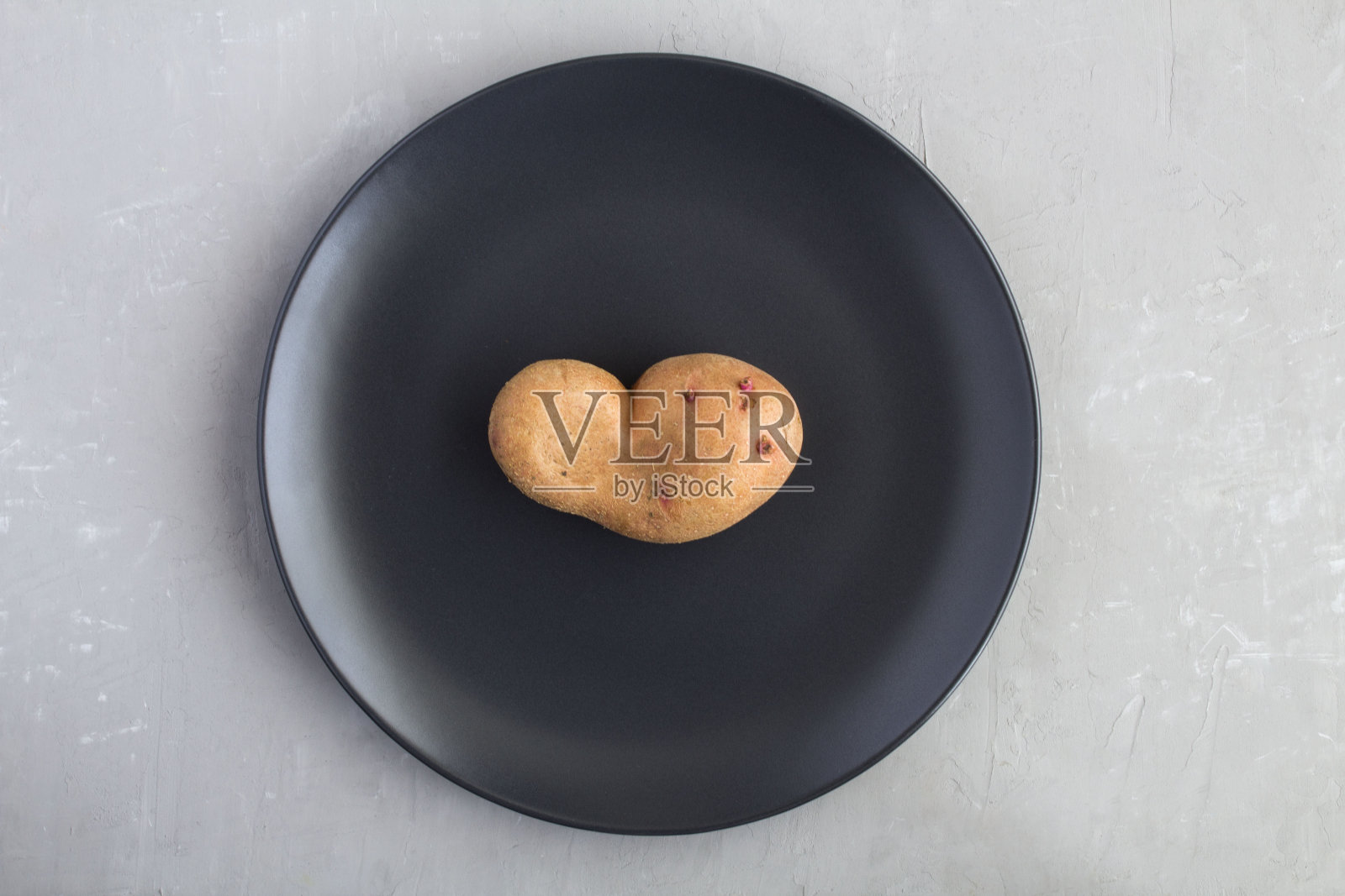 丑陋的食物。在灰色混凝土背景中央的一个黑色盘子上的丑陋的土豆。前视图。副本的空间。照片摄影图片