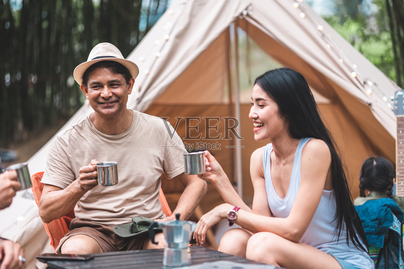 夏季露营在山上，以云杉林为背景。后景一群游客围坐在篝火旁休息，享受帐篷附近的新鲜空气。全家欢度假期，一起玩。照片摄影图片