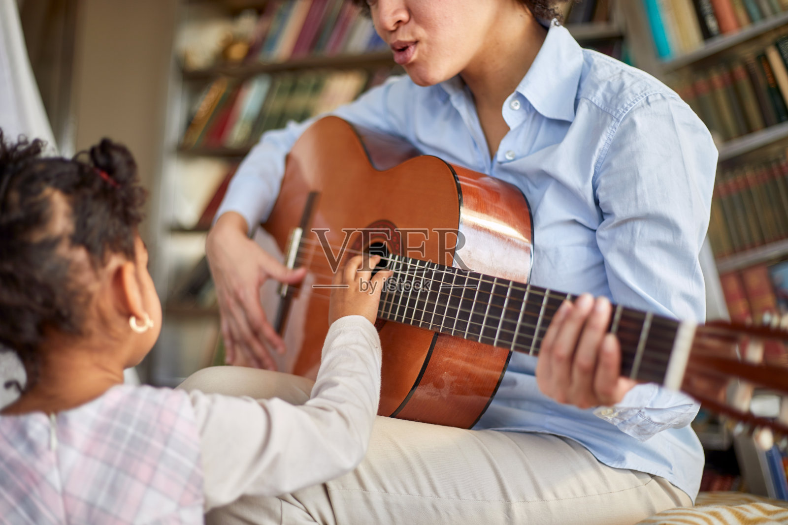 一个可爱的小女孩是如此感兴趣的母亲弹吉他，而花时间在家里一起。家庭,家里,游戏时间照片摄影图片