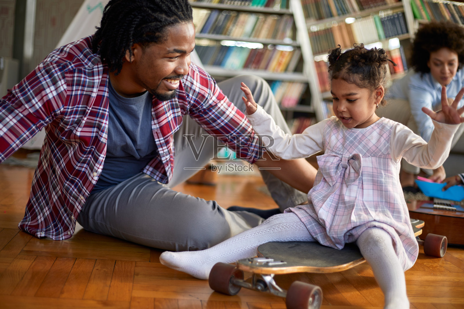 一个可爱的小女孩有一个美好的时间骑在滑板在家里和她的家人玩。家庭,家里,游戏时间照片摄影图片