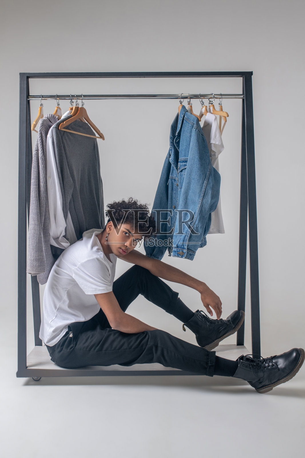 卷头发的年轻人坐在衣架旁边，穿着衣服，看起来很疲倦照片摄影图片