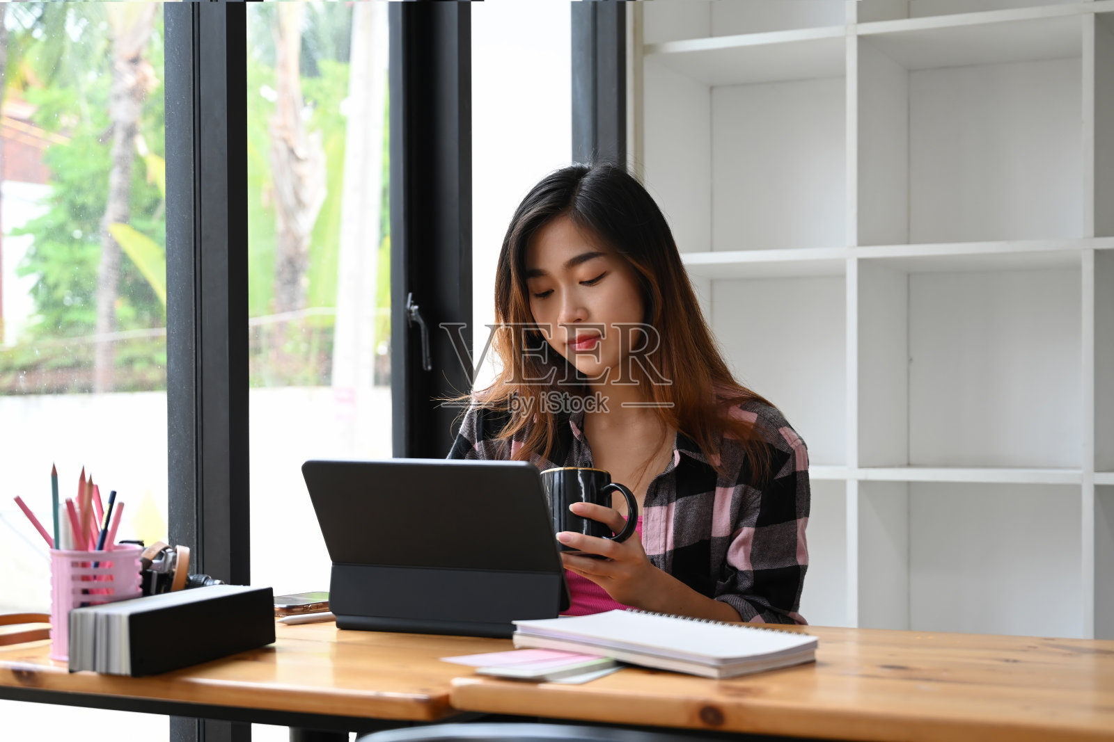 年轻女子创意设计师拿着咖啡杯和工作在电脑平板电脑在办公室。照片摄影图片