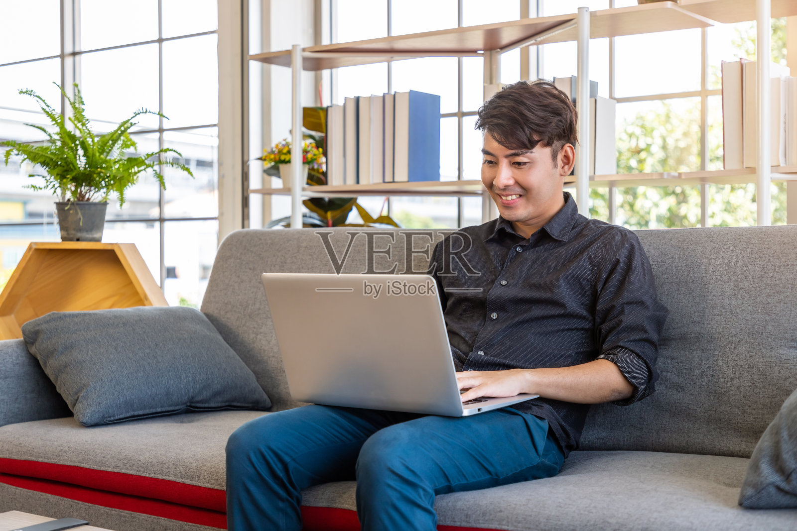 年轻的亚洲商人坐在客厅的沙发上用笔记本电脑在家工作，与同事在线开会。照片摄影图片