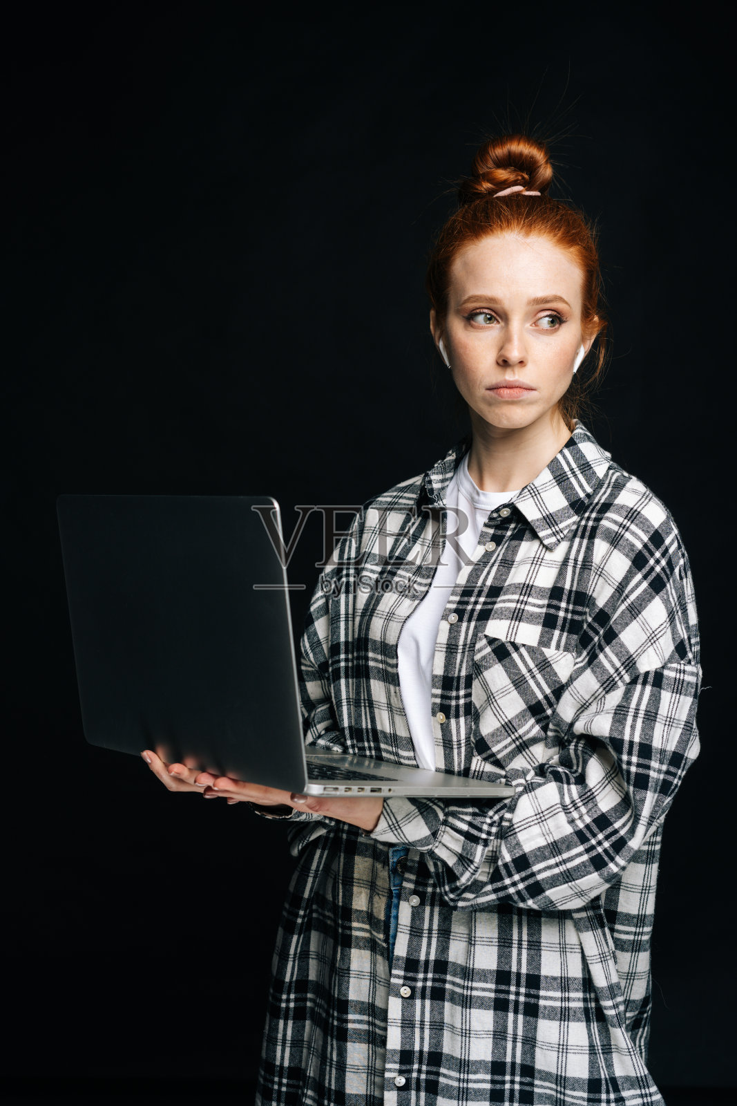 心烦意乱的年轻女子拿着手提电脑，戴着无线耳机，看向别处。照片摄影图片