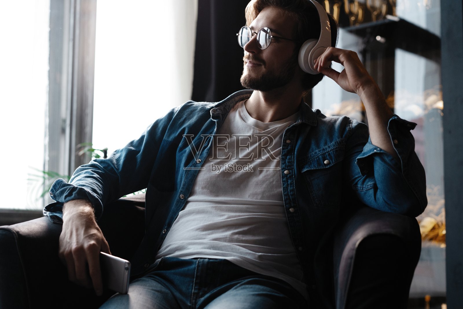 微笑的年轻成年男子戴着无线耳机在智能手机上听手机音乐照片摄影图片