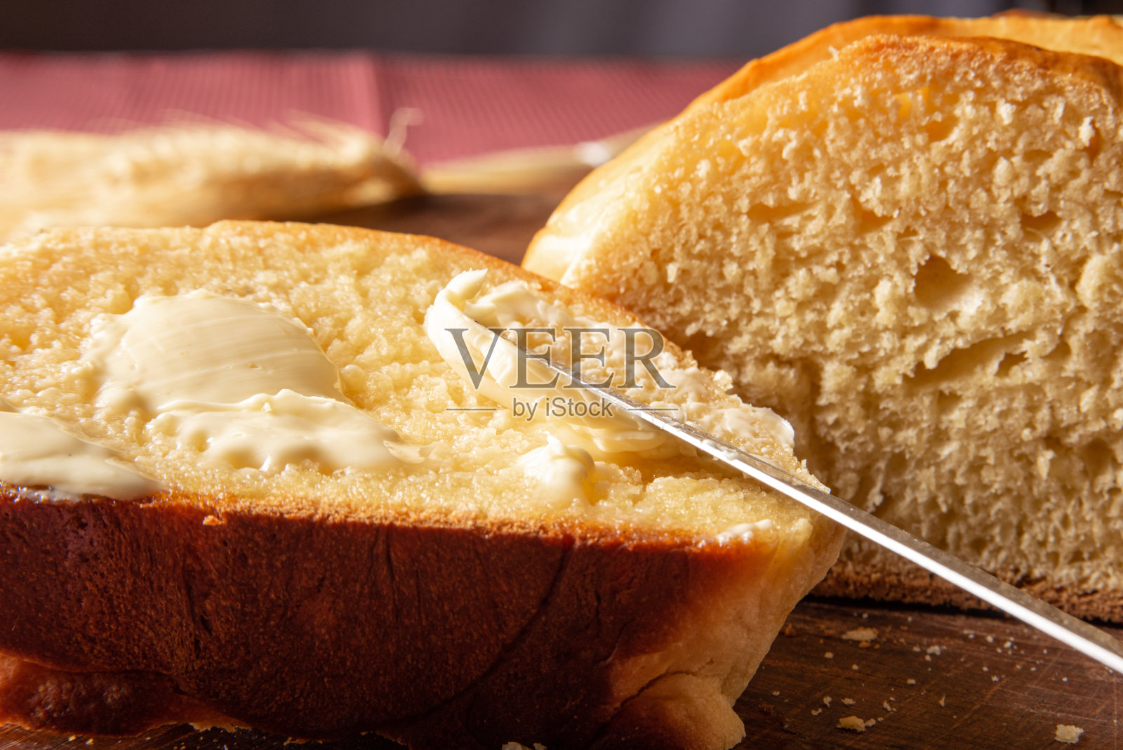 自制面包，把自制面包切成薄片，用黄油涂在木头上，一块红白格子桌布，一把小刀和一束小麦，选择性聚焦。照片摄影图片