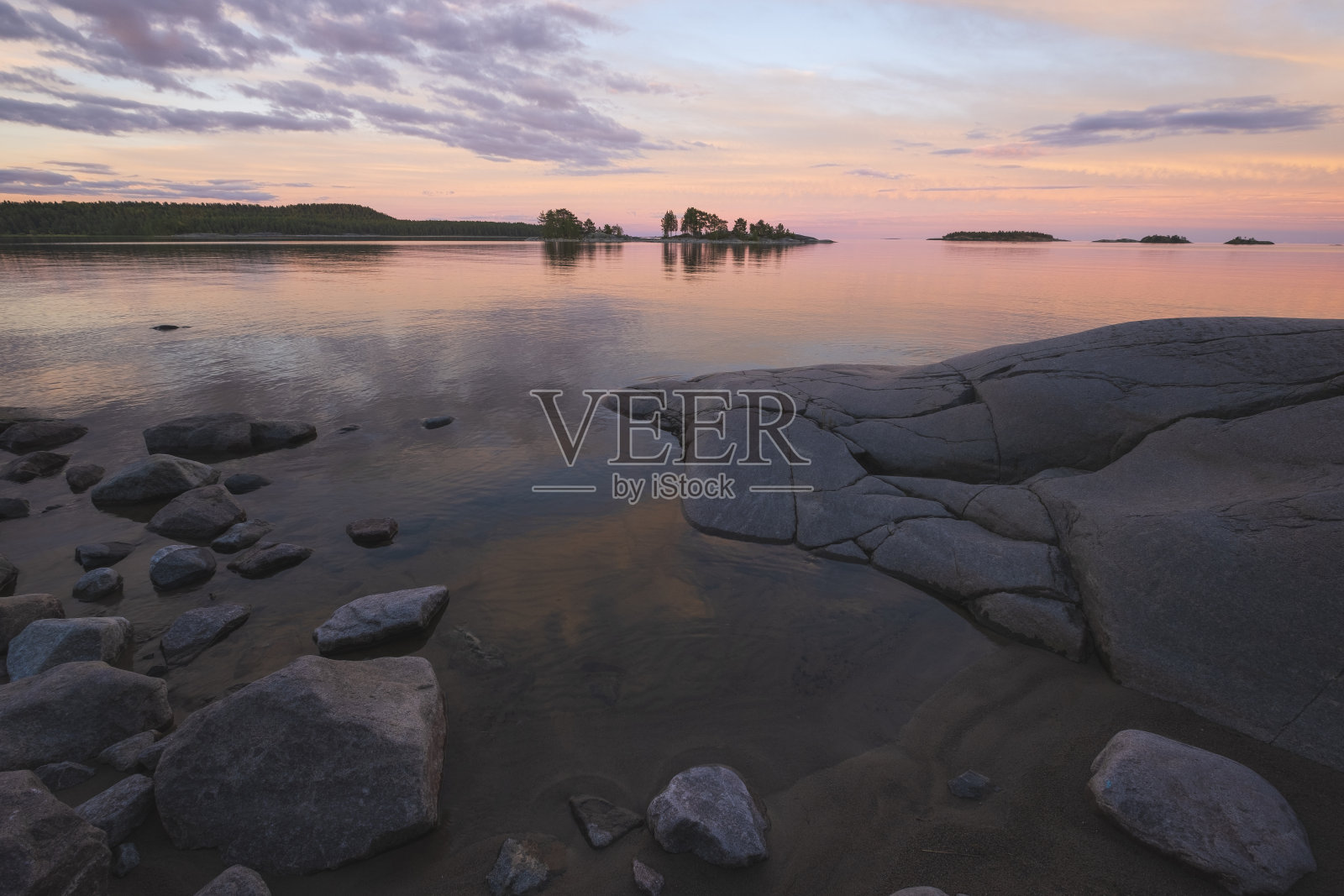 在俄罗斯卡累利阿的拉多加湖上美丽的粉红色日落在夏天的拉多加斯克里斯国家公园。岸边有水石、石岛和森林等自然景观照片摄影图片