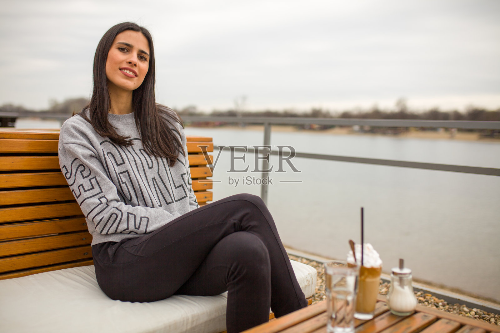 一个年轻女子，坐在河边附近的咖啡馆里。照片摄影图片