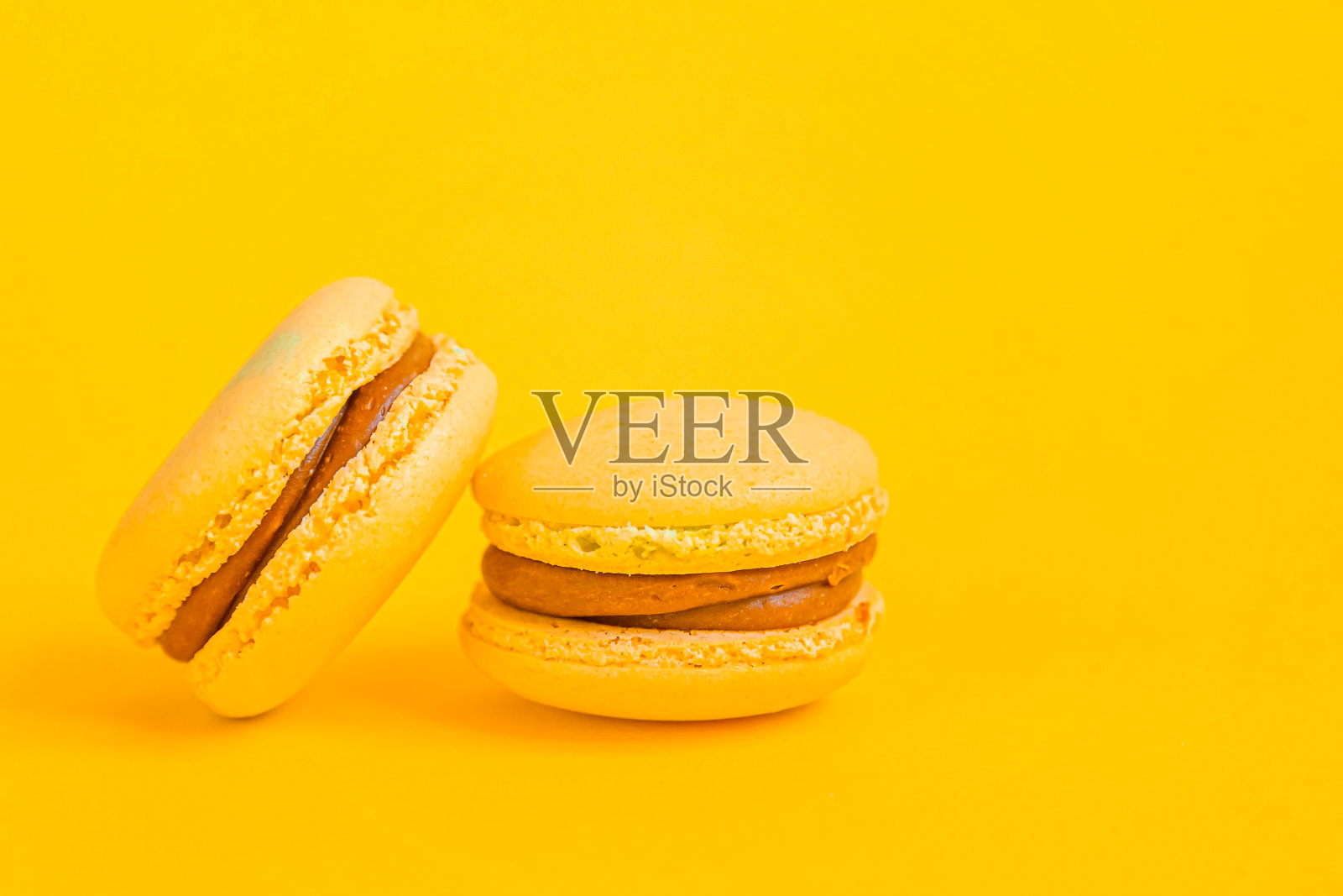 甜杏仁彩色黄马卡龙或杏仁龙甜品蛋糕孤立在时髦的黄色现代时尚背景。法国甜的饼干。最小的食品烘焙概念拷贝空间照片摄影图片